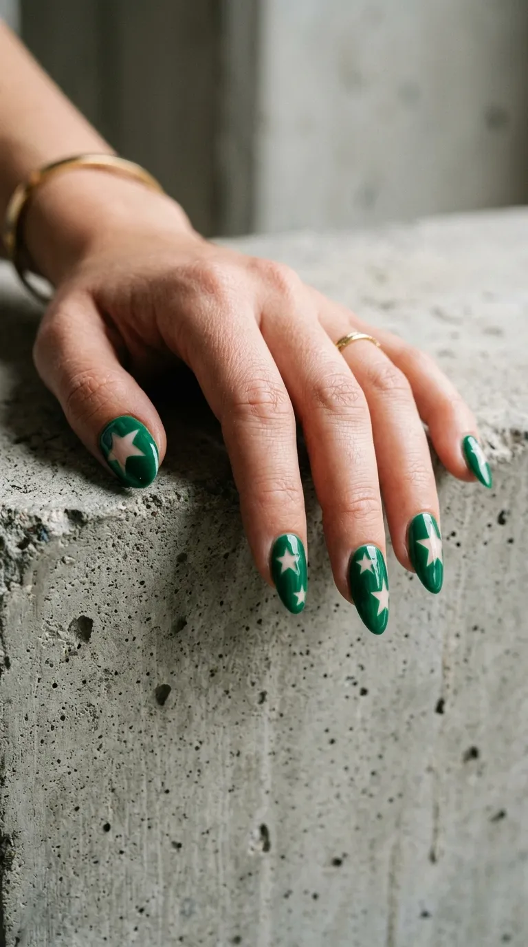 A contemporary photograph of medium-length nails with sections of bare natural nail showing through in star shapes, while the rest of the nail is painted in a rich emerald green. The bare nail areas create star silhouettes against the green background. The hand rests on a concrete surface. Modern, editorial lighting with slight shadow play. Shot on a DSLR, f/2.8.